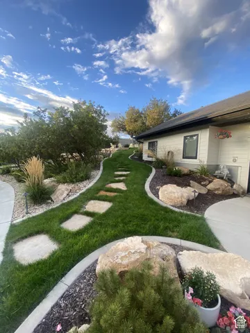 Manicured lawn with a stone-paver walkway, extensive landscaping featuring boulders and plantings, and a concrete perimeter