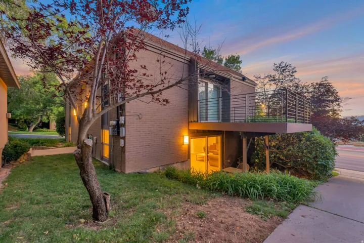 Brick exterior featuring a private balcony with horizontal railings, ground-level patio access, and mature landscaping