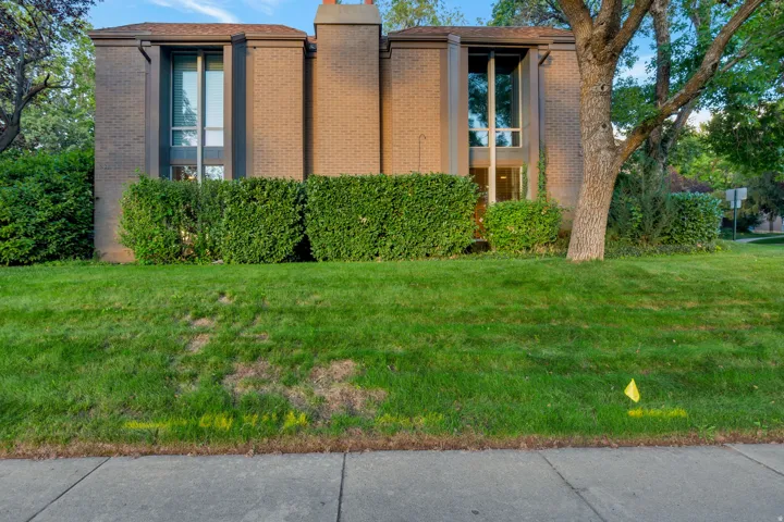 Brick exterior with large windows, mature trees, and established shrubs
