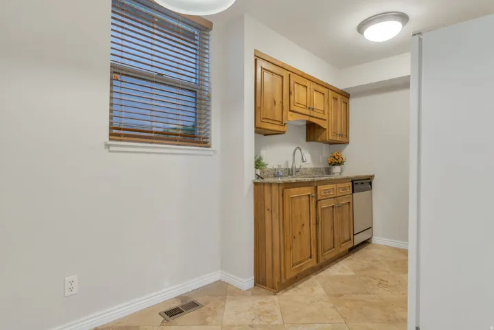 Wood-finish cabinetry, stone-finish countertop, stainless steel dishwasher, tile flooring, and a flush-mount ceiling light