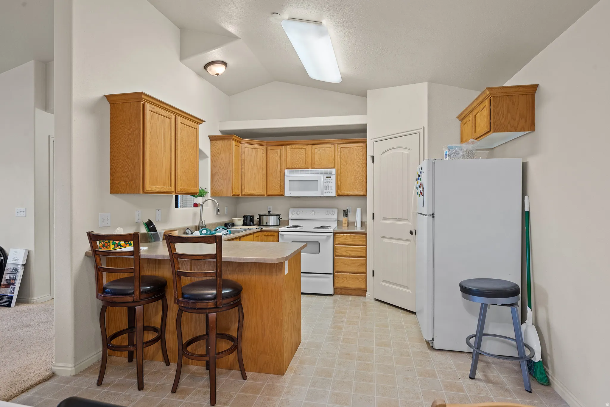 Kitchen featuring wood-finish cabinetry, white appliances, a breakfast bar, and vaulted ceilings