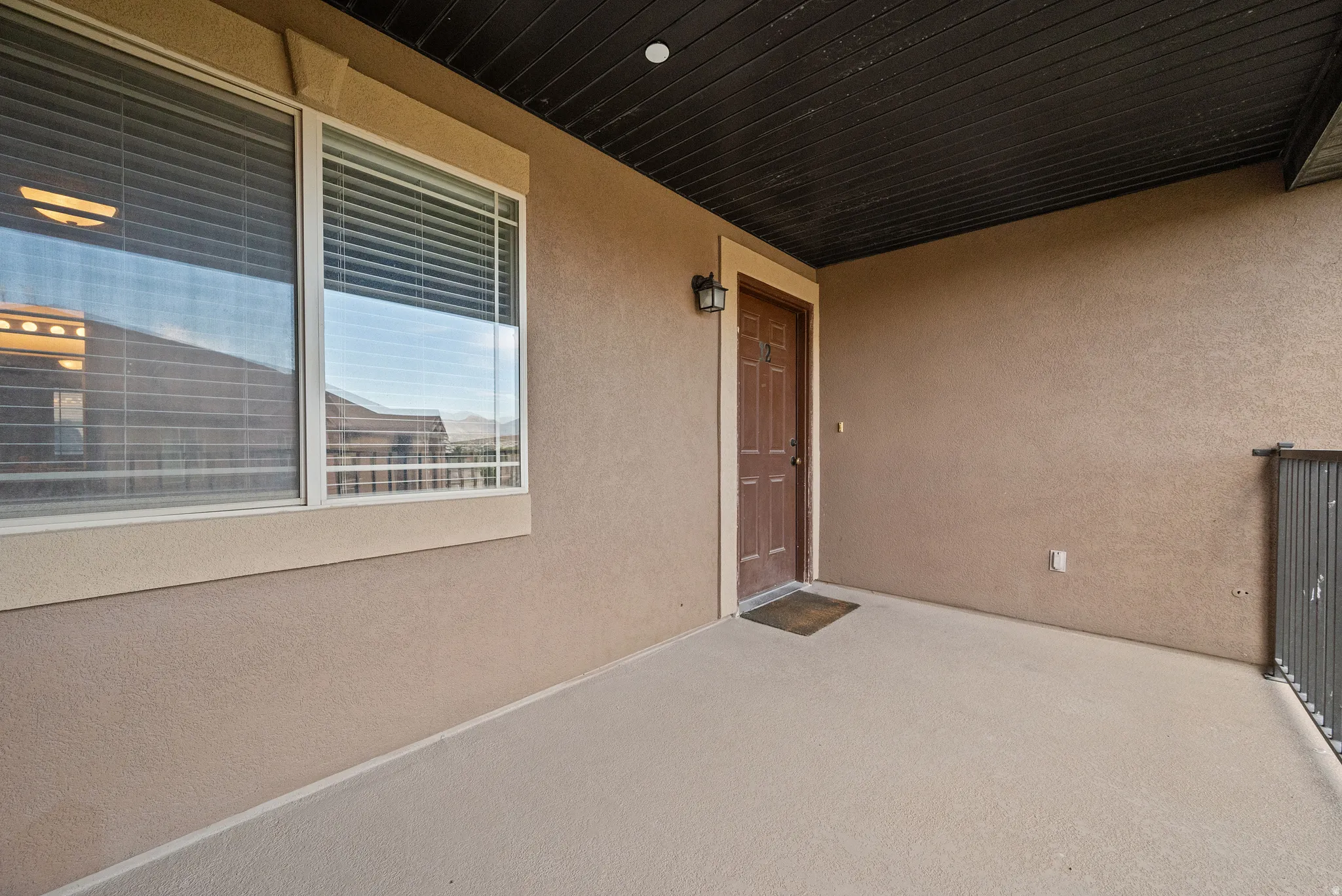 Covered outdoor patio featuring a textured stucco exterior, an exterior light fixture, a paneled entry door, and a metal railing