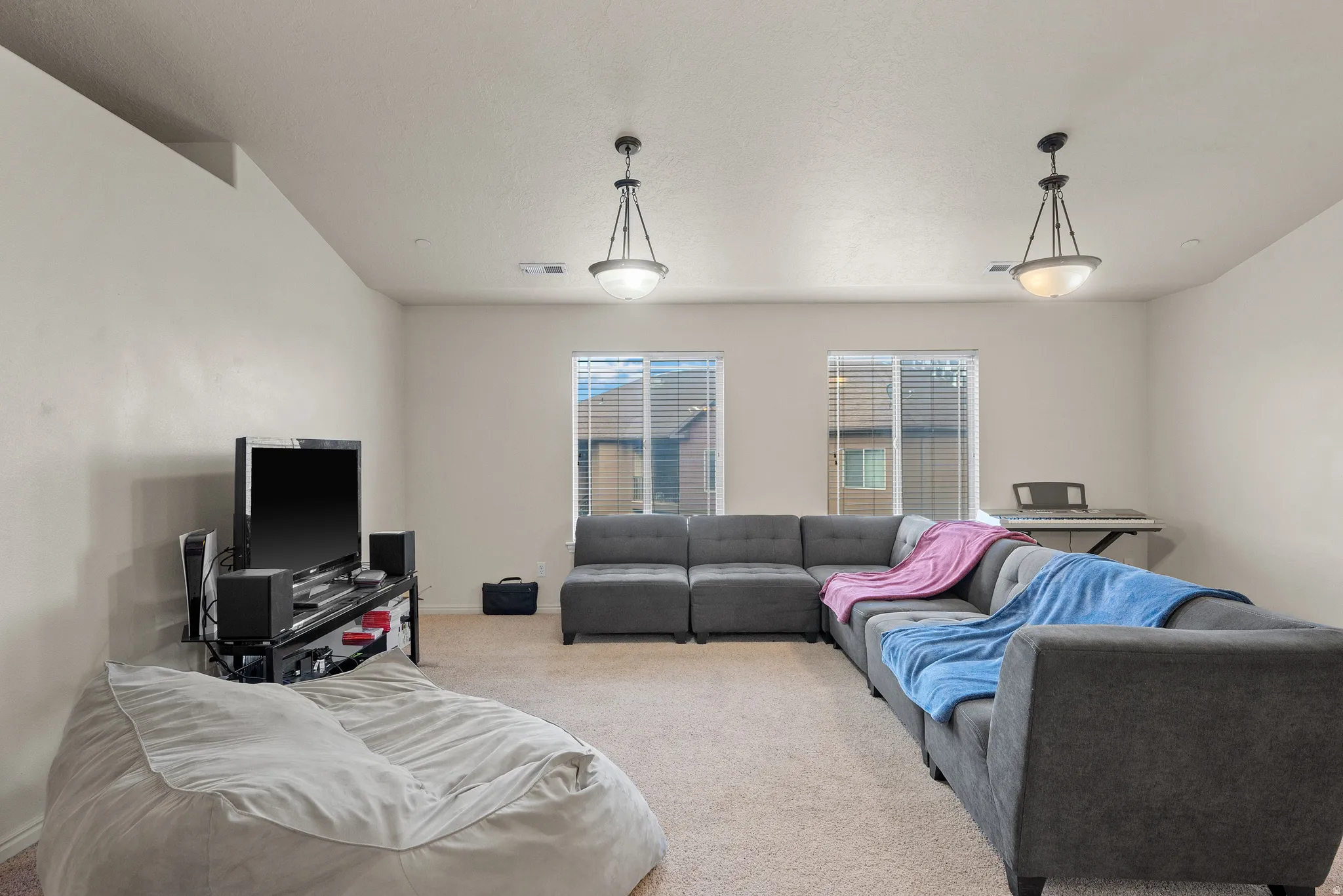 Carpeted flooring with painted walls, multiple windows with blinds, and pendant lighting fixtures