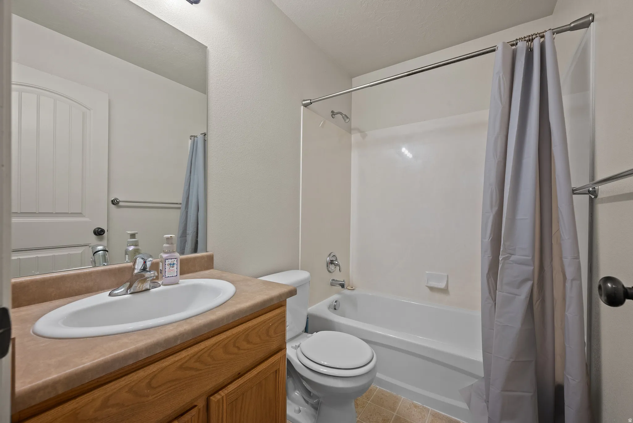 Bathroom featuring a wood-finish vanity with a laminate countertop, an undermount sink, a toilet, a bathtub with a shower, and tile flooring