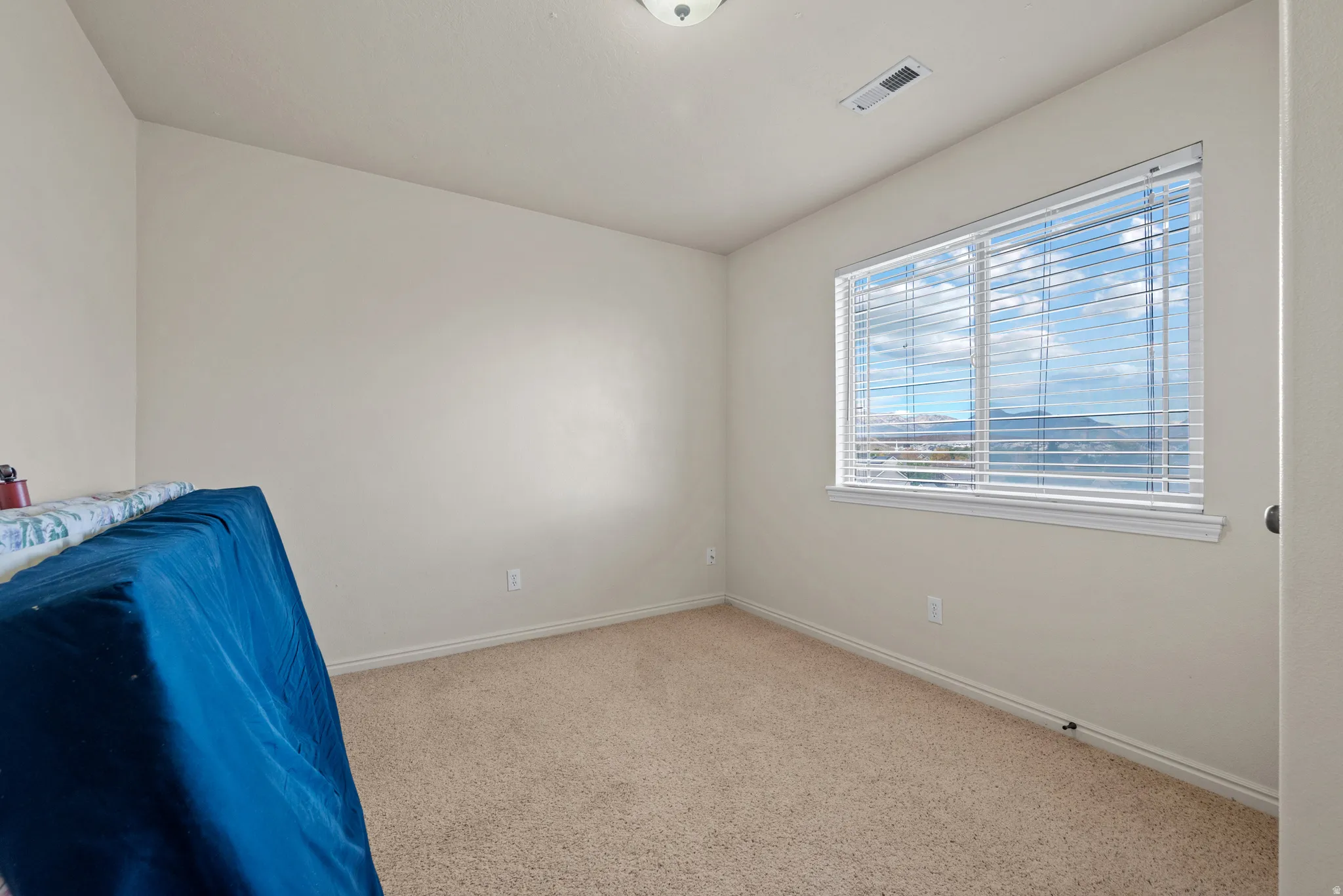 Neutral wall color, wall-to-wall carpeting, and a large window with horizontal blinds
