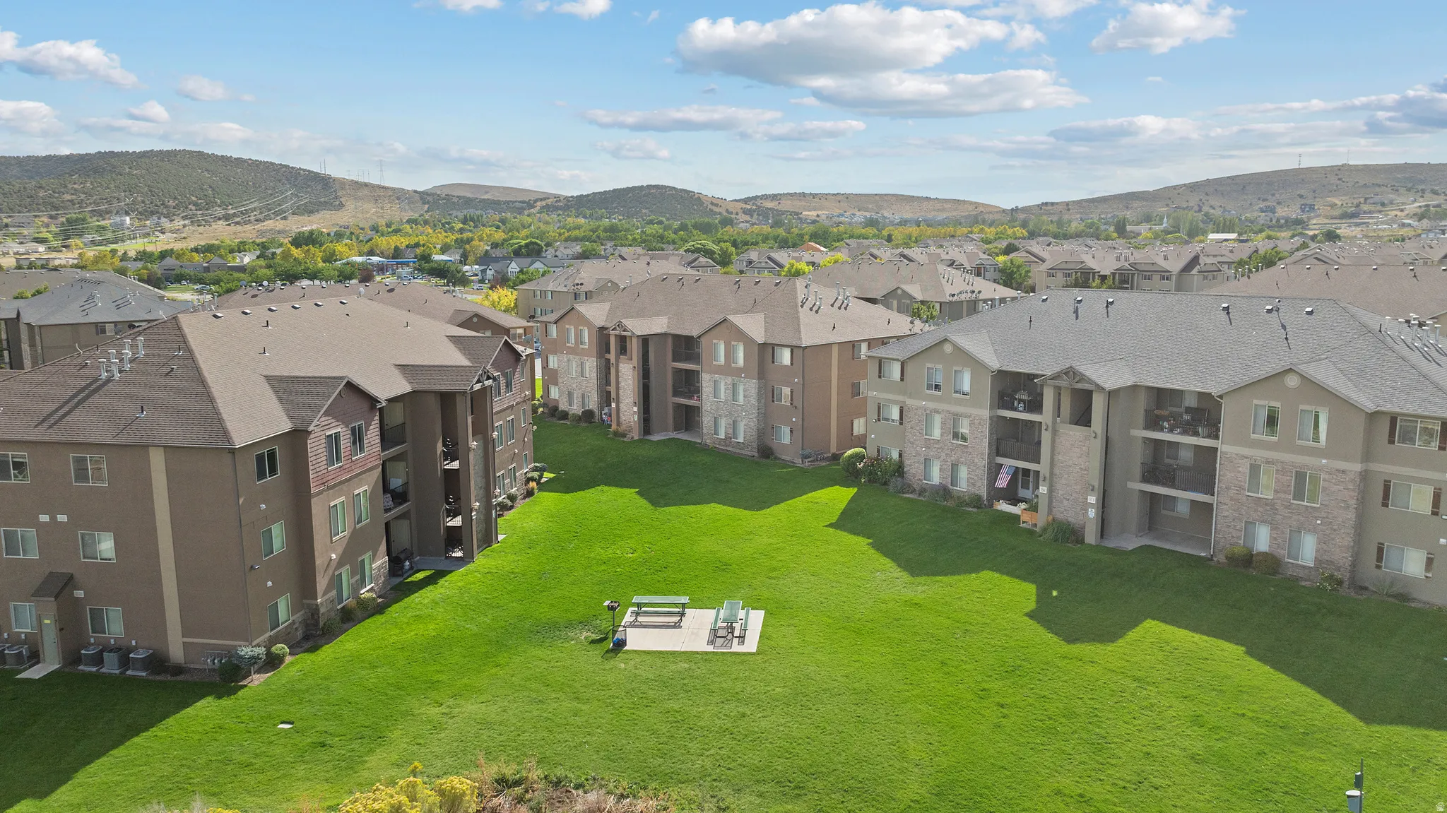 Expansive green space with a paved patio and picnic area, surrounded by multi-story residential buildings featuring balconies
