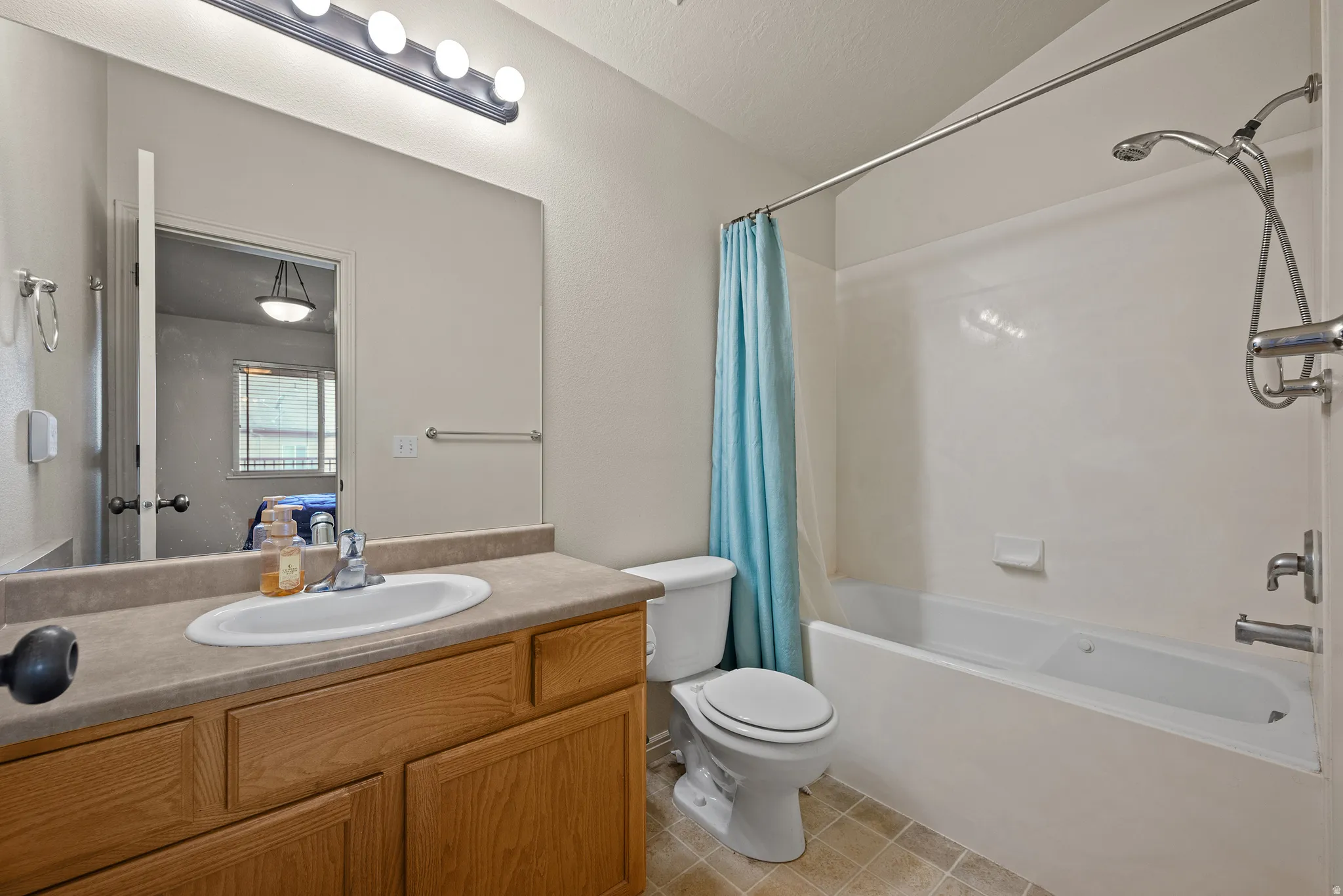 Bathroom featuring an integrated bathtub and shower, a single-sink vanity with wood-finish cabinetry, a large wall-mounted mirror, and tile flooring
