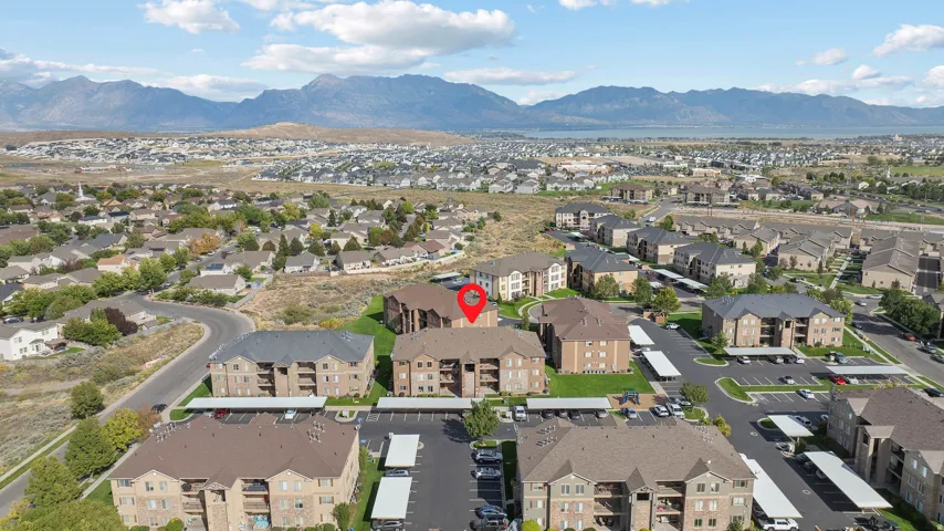 Community with multiple multi-story buildings, covered parking structures, and paved roadways, set against a mountain and lake backdrop