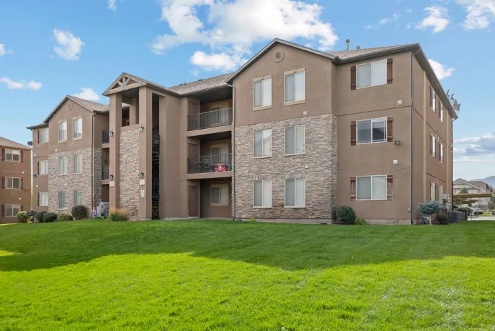Exterior facade featuring stucco and stone veneer, multiple balconies with metal railings, and a manicured lawn