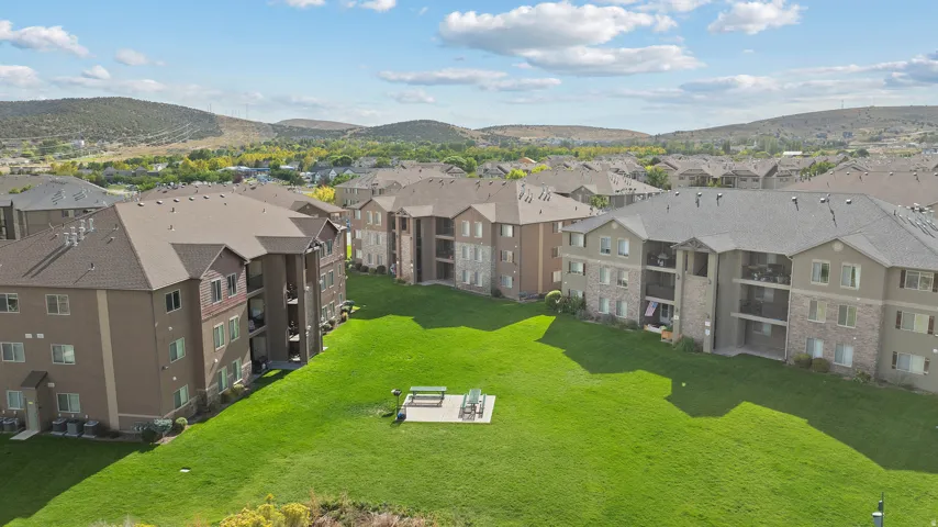 Expansive green space with a paved patio and picnic area, surrounded by multi-story residential buildings featuring balconies