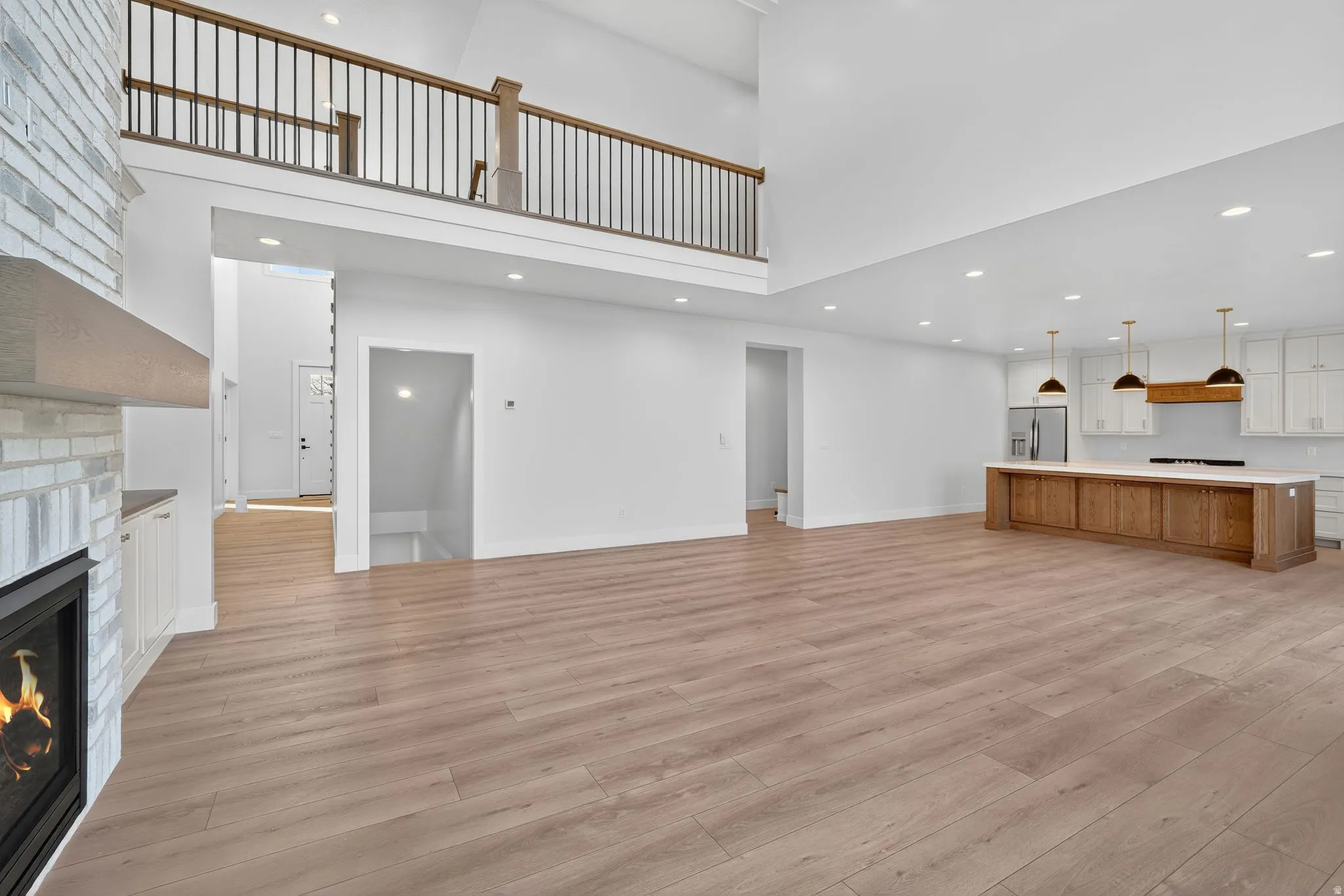 Open concept living space featuring wood-finish flooring, a white brick fireplace, a kitchen island with integrated cabinetry, and recessed lighting