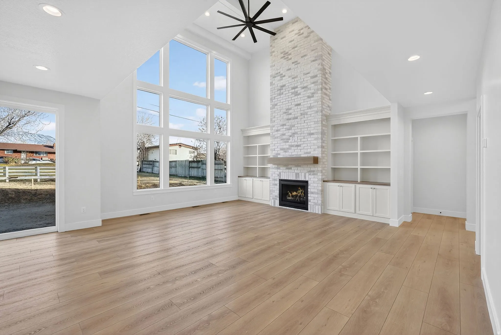 Vaulted ceilings, a full-height brick fireplace, built-in shelving, wood-finish flooring, and large picture windows