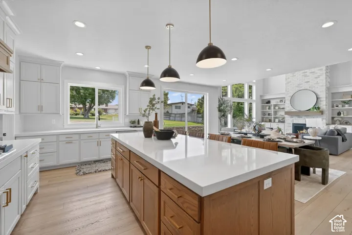 Spacious kitchen island with white countertop, white cabinetry with gold-toned hardware, wood-finish flooring, recessed lighting, and large windows