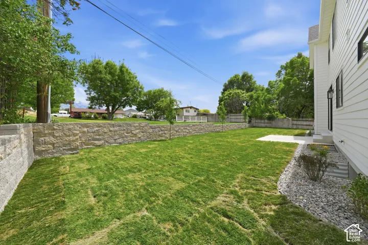Expansive lawn area with a stone retaining wall and concrete patio
