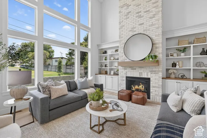 Two-story windows, a white brick fireplace with a wood mantle, built-in shelving, and wood-finish flooring