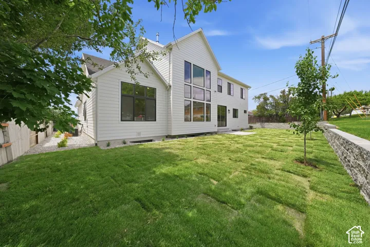 Contemporary white siding exterior with a multi-pane window wall, black-framed windows, a walkout door, and a stone retaining wall