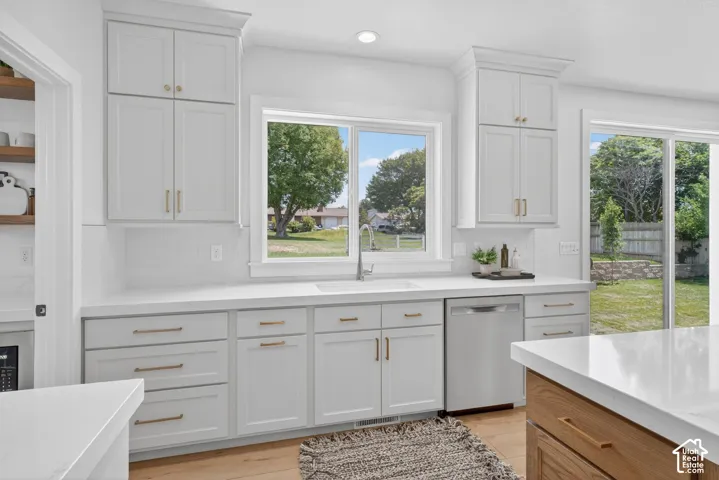 White shaker cabinetry with gold-finish hardware, stainless steel dishwasher, white countertop, white subway tile backsplash, and wood-finish flooring