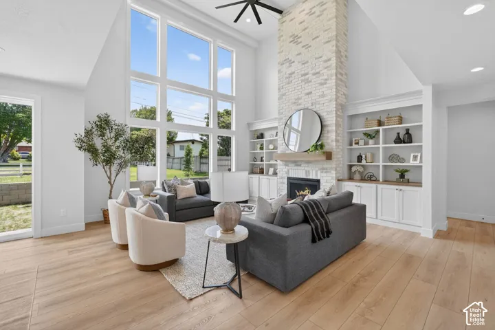 Two-story vaulted ceiling with large windows, light wood-finish flooring, white brick fireplace with a wood mantle, and built-in white cabinetry with open shelving