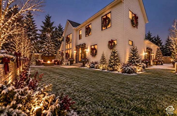 White-sided residence with multiple large windows, an exterior fireplace, and mature evergreen landscaping