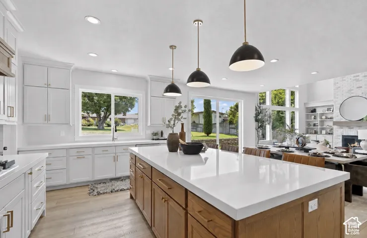 White cabinetry with gold-tone hardware, wood-finish flooring, recessed lighting, expansive center island with white countertop, and black pendant lighting fixtures