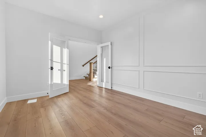 Wide plank wood-finish flooring, custom wall molding, recessed ceiling lighting, and French doors with glass panels
