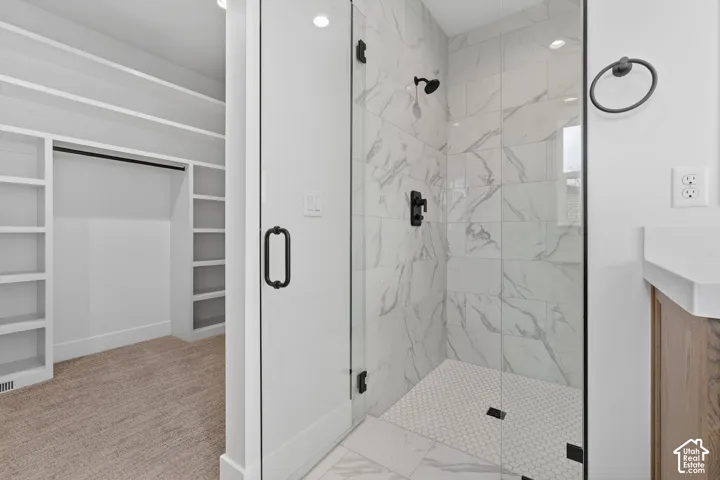 Primary bathroom featuring a frameless glass-enclosed shower with marble-look tile surround, hexagonal mosaic floor tile, dual showerheads with matte black fixtures, and a wood-finish vanity with integrated sink and countertop