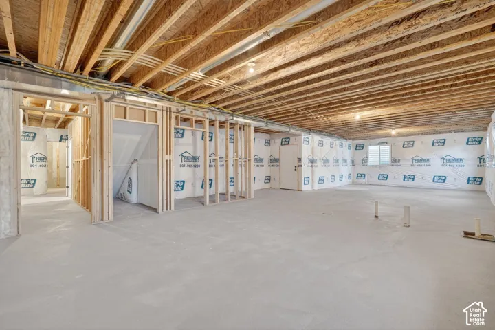 Unfinished basement with exposed ceiling joists, framed interior walls, concrete flooring, and multiple windows