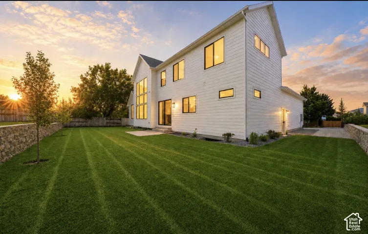 White board and batten exterior with expansive windows, manicured lawn, stone retaining wall, and concrete patio