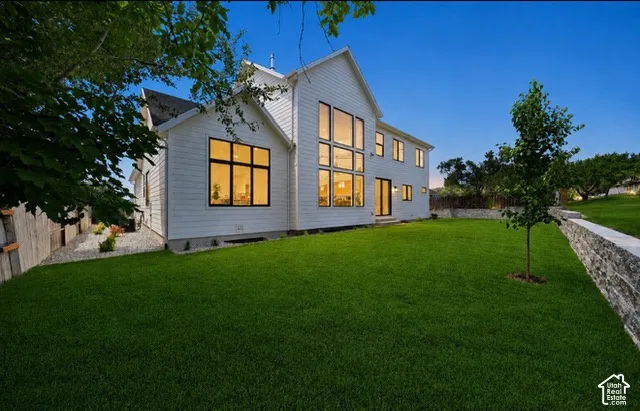 Modern farmhouse architecture with vertical and horizontal siding, extensive multi-story windows, a glass-paneled door, and a spacious lawn with a stone retaining wall