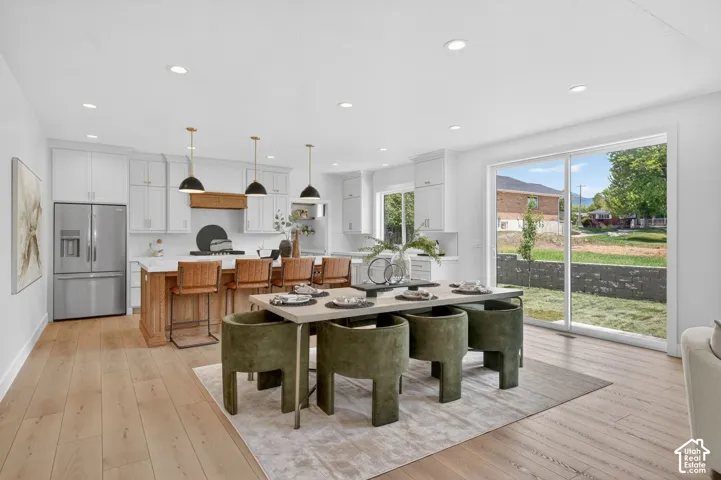 Open-concept kitchen and dining area featuring light wood-finish flooring, white cabinetry, a large kitchen island with counter seating, and stainless steel appliances