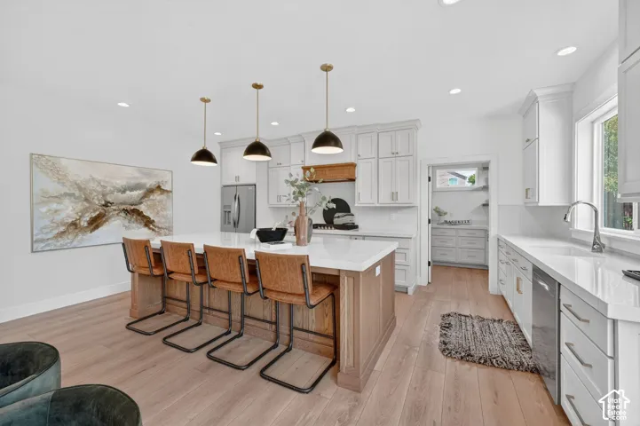 Spacious kitchen featuring an expansive center island, light wood-finish flooring, white cabinetry, recessed lighting, and stainless steel appliances
