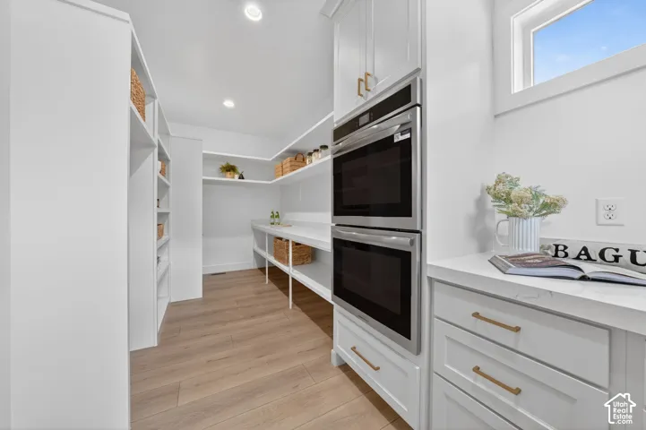 Built-in double ovens, extensive white cabinetry, gold-tone hardware, wood-finish flooring, and white countertops