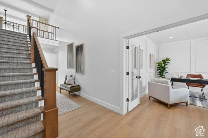 Hardwood-style flooring throughout, staircase with carpeted treads and wood newel posts, white walls, and an office space featuring paneled wall detailing and French doors