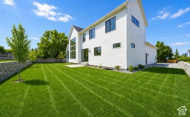White siding exterior with black-framed windows, a prominent gable, a concrete patio, and a stone retaining wall