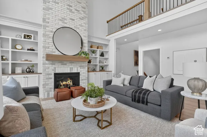Two-story living area featuring a light-colored brick fireplace with a wood mantle, built-in shelving and cabinetry, and a second-level open railing