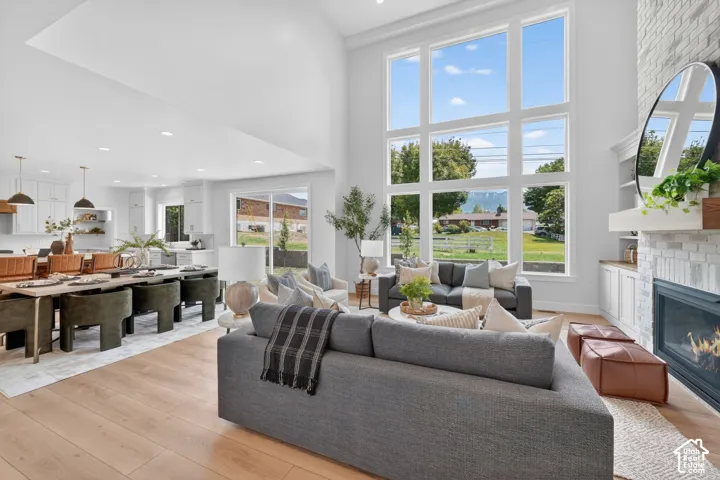 Open-concept living area with soaring ceilings, expansive windows, a white brick fireplace, and wood-finish flooring