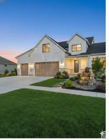 Modern farmhouse exterior featuring board and batten siding, two-car garage with wood-finish doors, stone accents, and a tiered rock water feature