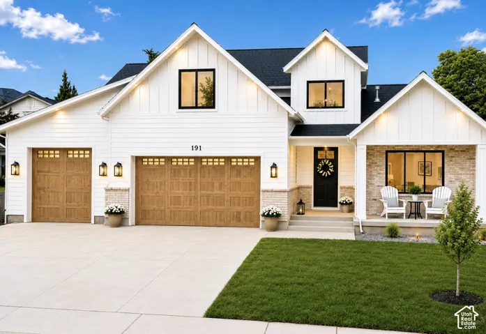 White siding exterior with black-framed windows, wood-finish garage doors, brick accents, and a covered porch