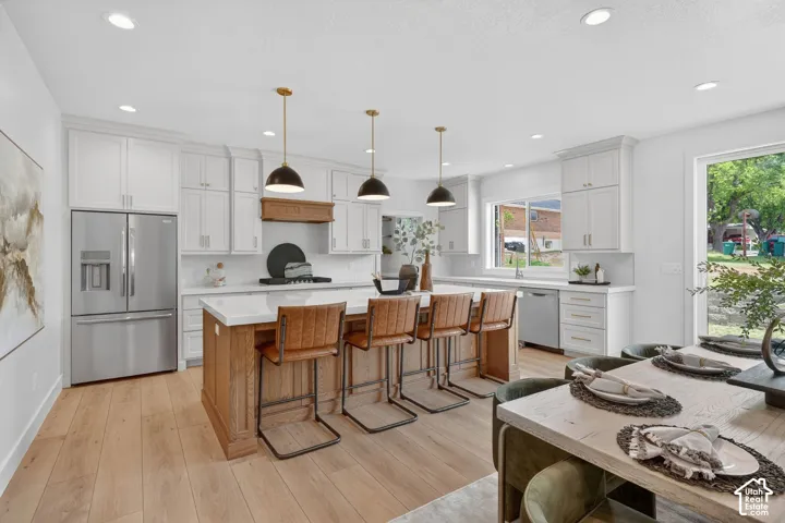 Open-concept kitchen featuring white cabinetry, stainless steel appliances, a wood-finish island with seating, and wood-finish flooring