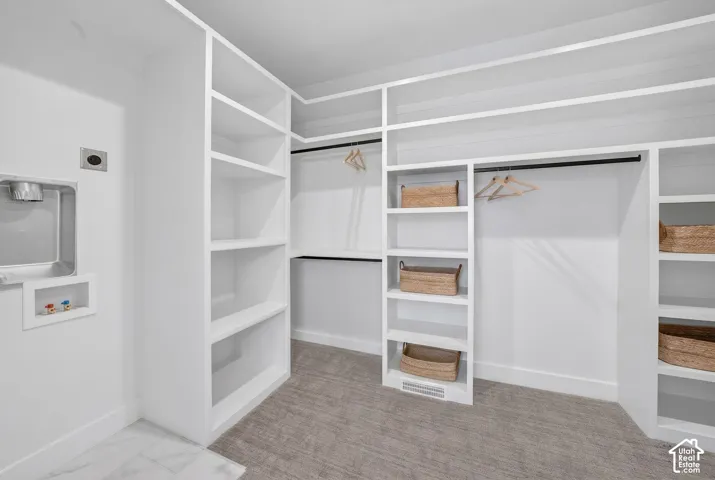 Integrated laundry hookup with white marble-style flooring, extensive built-in shelving, black hanging rods, and gray patterned carpeting