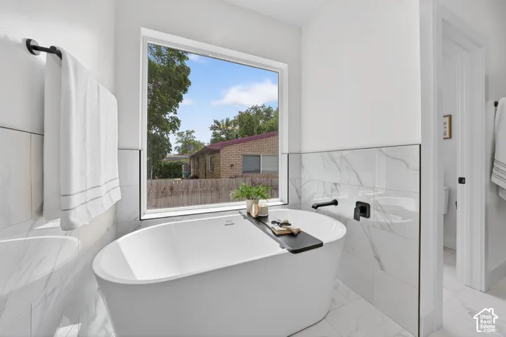 Freestanding soaking tub with matte black fixtures, set against large format tile walls and flooring