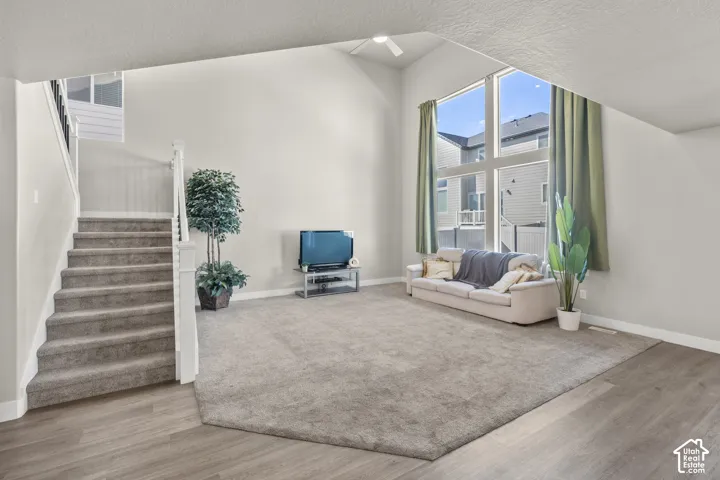 Vaulted ceiling with a ceiling fan, expansive windows, light wood-finish flooring, and carpeted stairs with white balusters