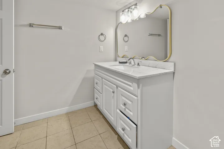 White vanity with multiple drawers and a single sink, light-colored countertop, wall-mounted mirror with an ornate frame, and tiled flooring
