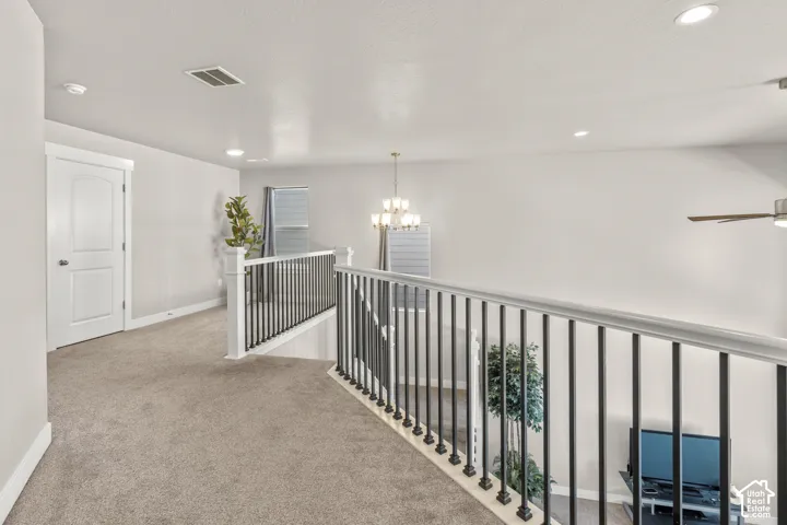 Carpeted hallway with a white panel door, recessed lighting, and a chandelier