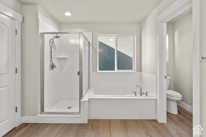 Glass-enclosed shower with a built-in shelf, deep soaking tub with brushed nickel fixtures, wood-finish flooring, and a window providing natural light