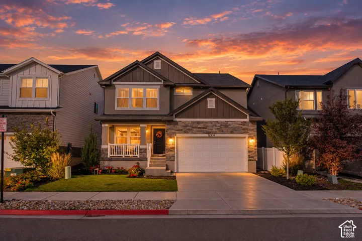 Two-story residence featuring a stone and stucco exterior, an attached two-car garage, and a covered front porch with white railing