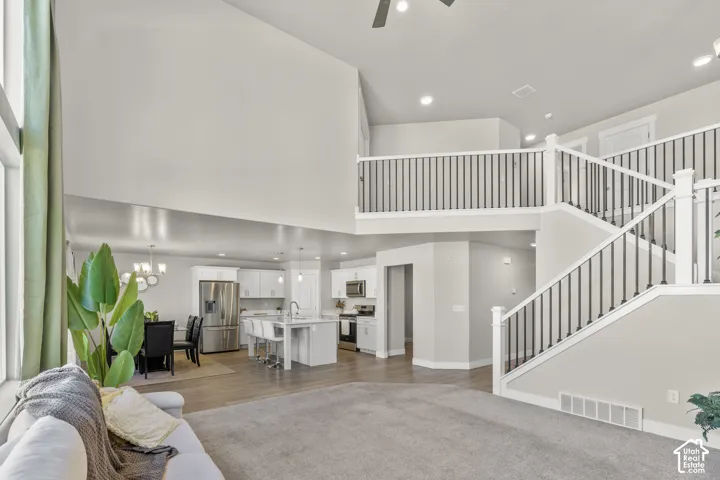 Vaulted ceilings with recessed lighting, two-story staircase with wrought iron balusters, white kitchen cabinetry, stainless steel appliances, and wood-finish flooring