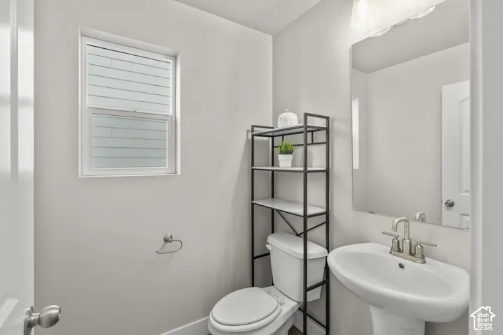 Pedestal sink with brushed nickel faucet, wall-mounted mirror, overhead lighting, single window, and toilet