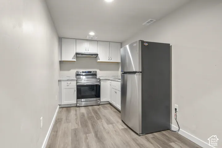 Corner kitchen featuring wood-finish flooring, white cabinetry, stainless steel appliances, and integrated overhead lighting