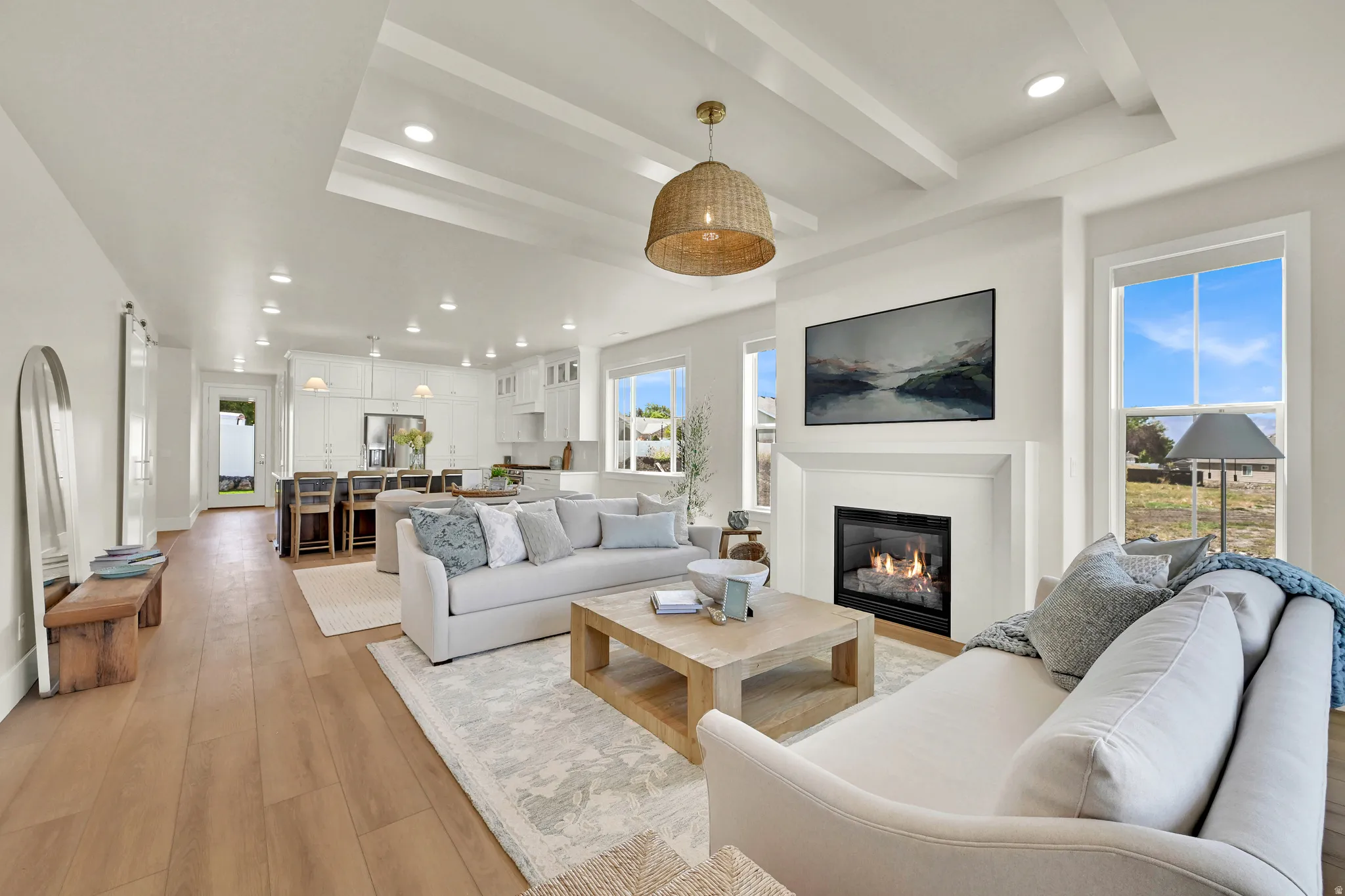 Open-concept living space featuring wood-finish flooring, a recessed ceiling with exposed beams, a built-in fireplace with mantel, and recessed lighting